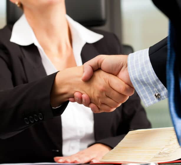 A close-up of a professional handshake between two individuals, one in a business suit and the other in a formal shirt with cufflinks